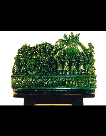 Detailed green stone artwork depicting a warrior in battle stance with traditional weapons