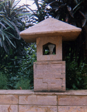 Traditional temple lamp stand with carved deity motifs and architectural details in durable natural sandstone material